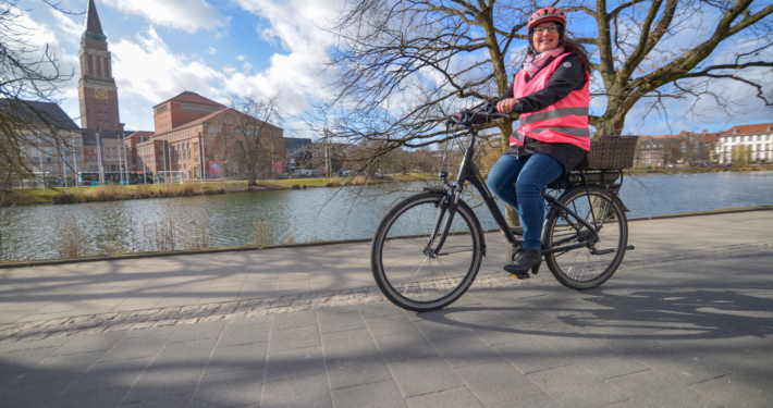 Silke Stolze auf ihrem E-Bike am kleinen Kiel samt Rathaus im Hintergrund