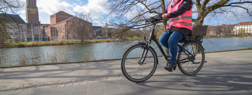 Silke Stolze auf ihrem E-Bike am kleinen Kiel samt Rathaus im Hintergrund